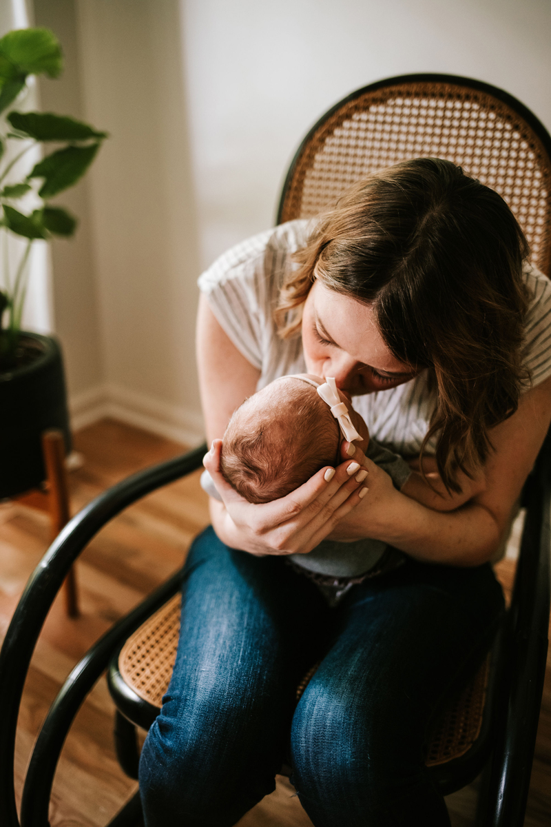 Atlanta Newborn Photographer, New mom sits in rocking chair kissing baby in her arms