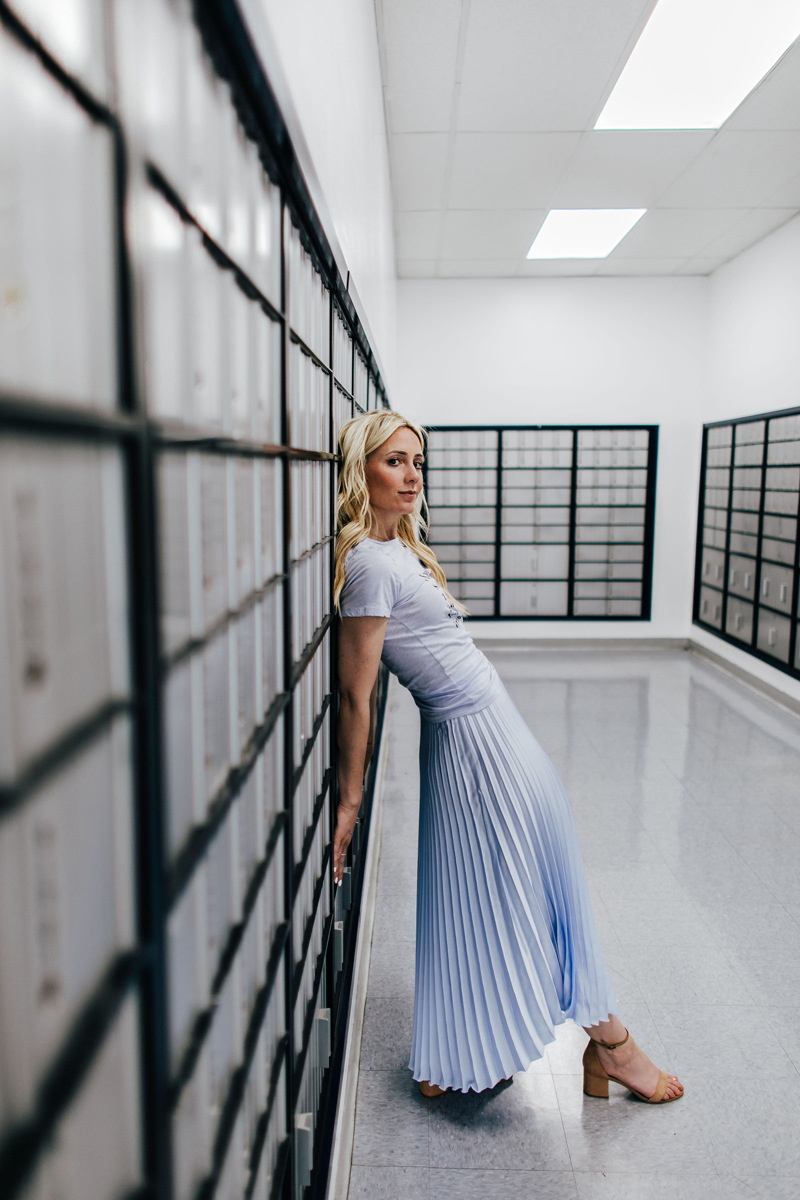 Atlanta Blogger-Influencer Photographer, Blonde slender woman in sky blue dress leans on wall of post office boxes