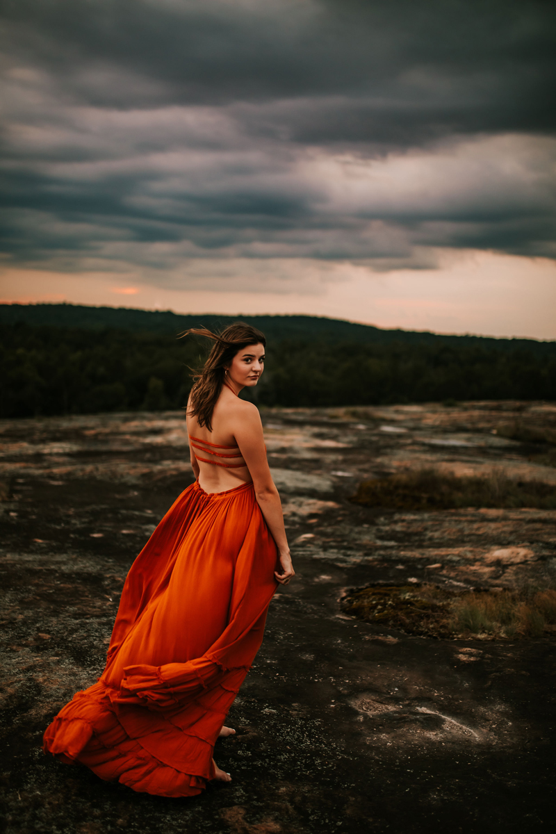 Atlanta Family Photographer, woman in flowing orange dress looks back as she walks toward forest
