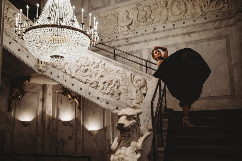 Atlanta Influencer-Blogger Photographer, woman leans back with her flowing black dress beside carved marble walls