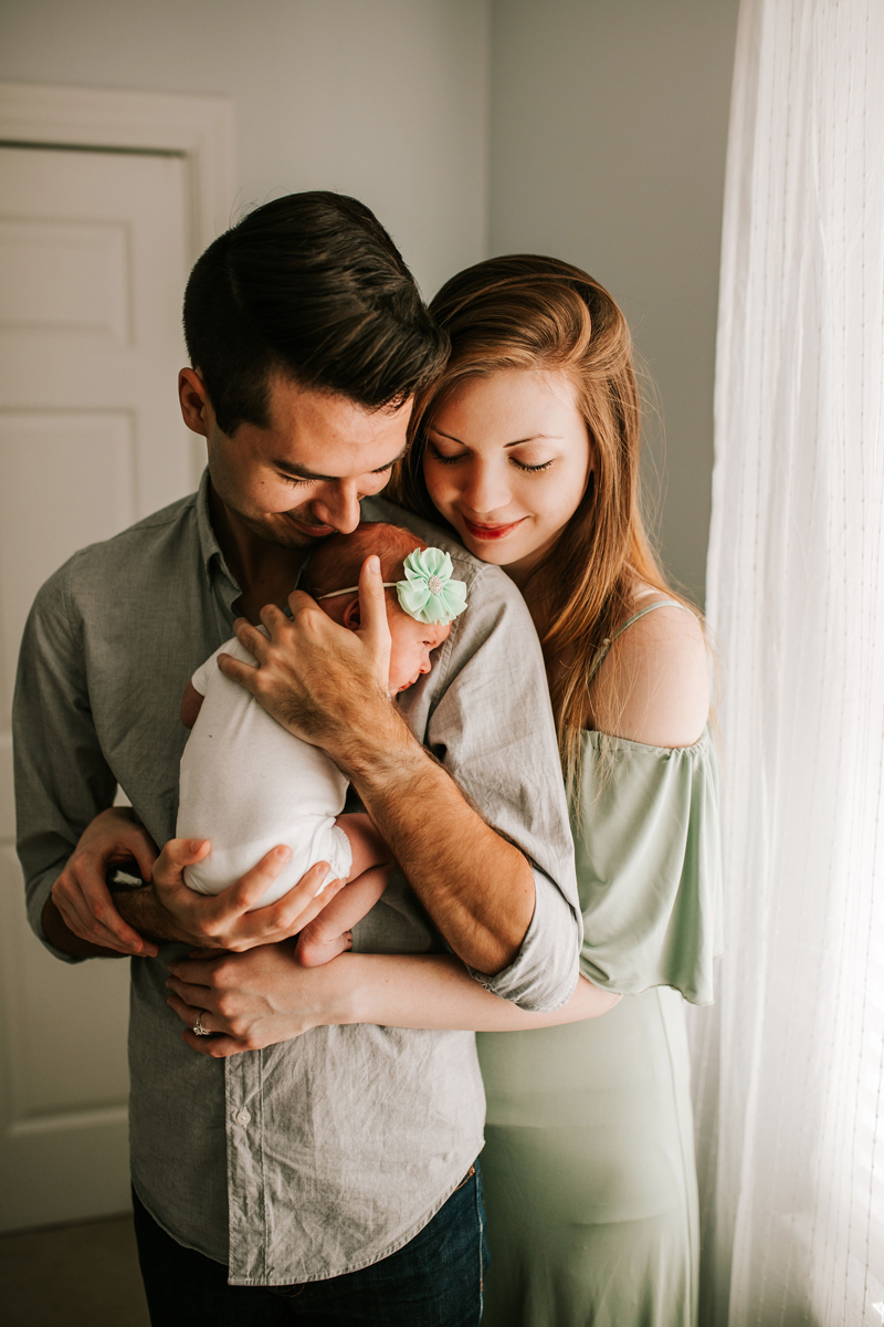 Atlanta Newborn Photographer, Mom hugs dad as he holds newborn daughter