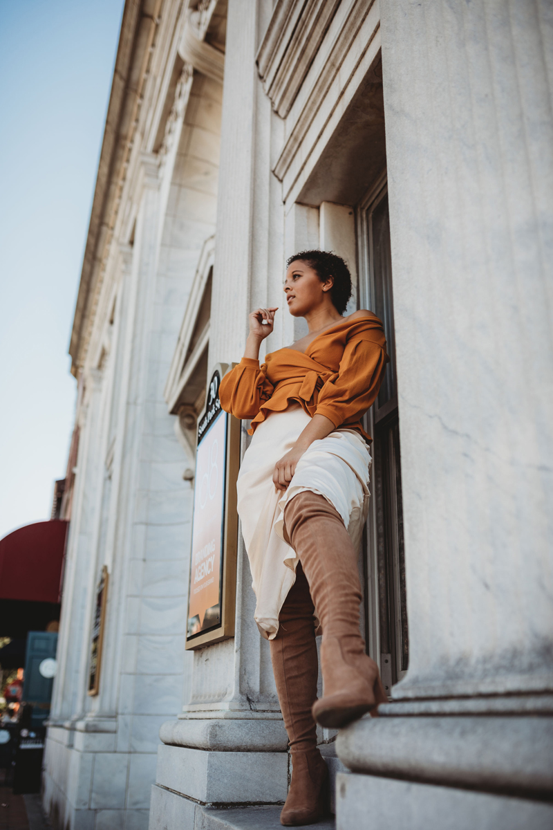 Atlanta Blogger-Influencer Photographer, In full fashion, woman leans against museum wall with burnt orange blouse