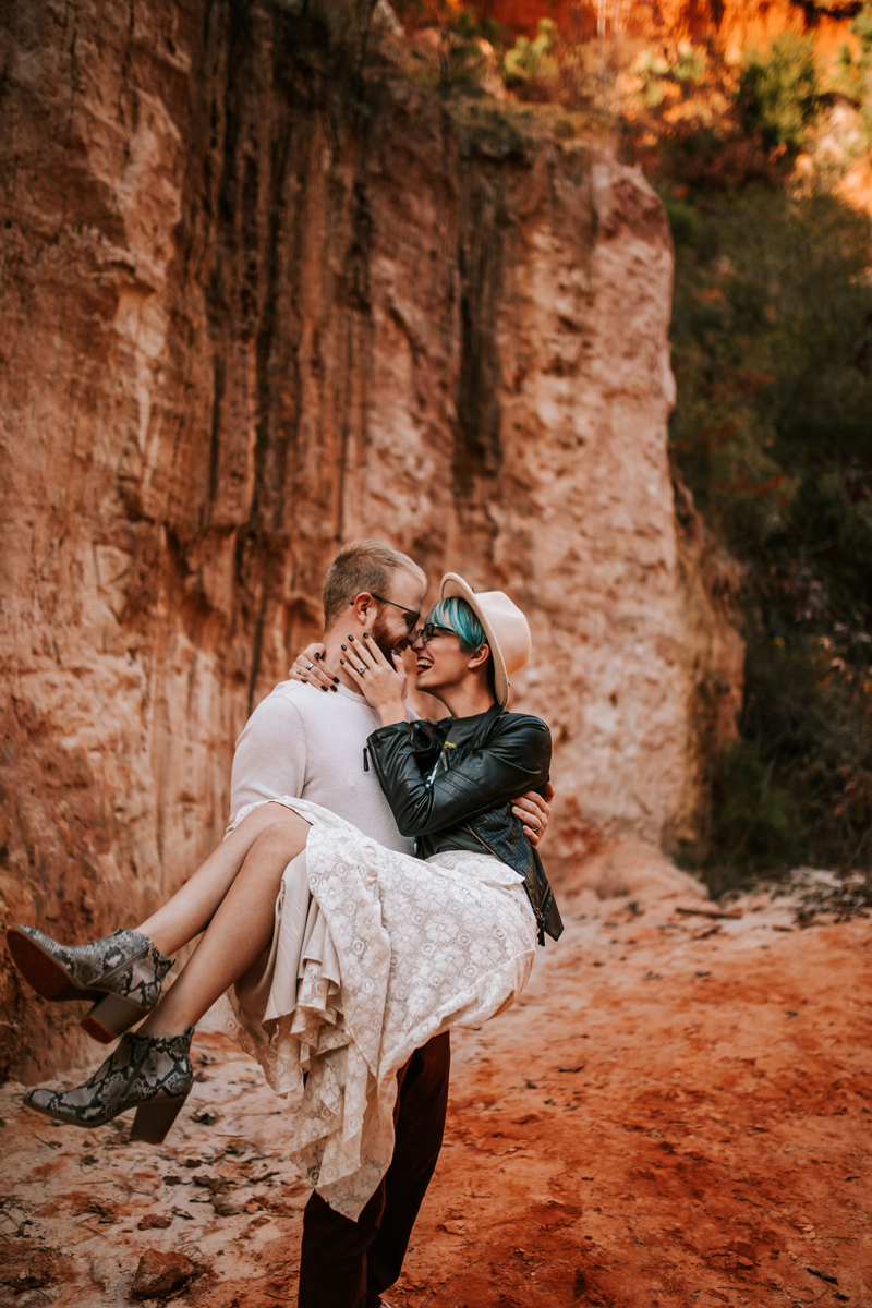Atlanta Couples Photographer,  man holds woman, they are nose to nose smiling before a red canyon wall