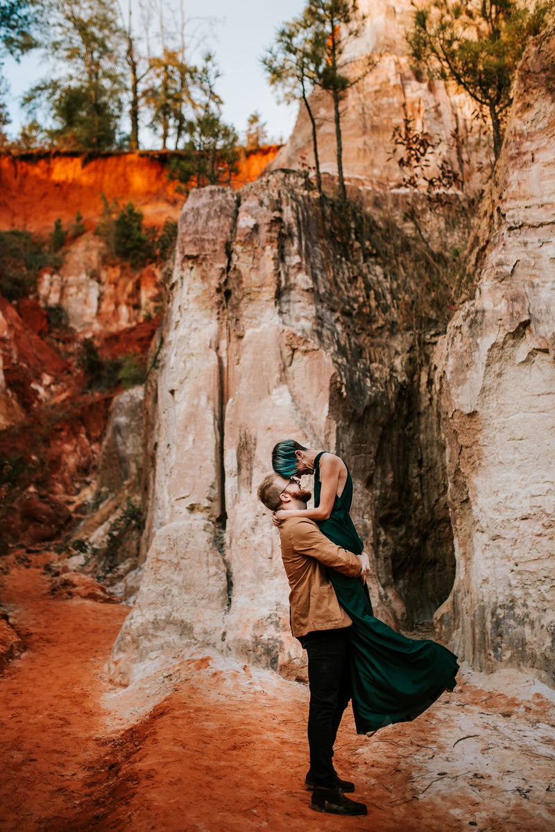 Atlanta Couples Photographer, man holds a woman near red and white canyon walls, she has vibrant green hair