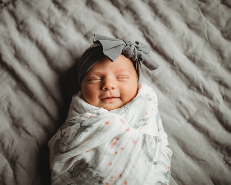 Atlanta Newborn Photographer, while cozily in a blanket, a little baby girl smiles in her sleep