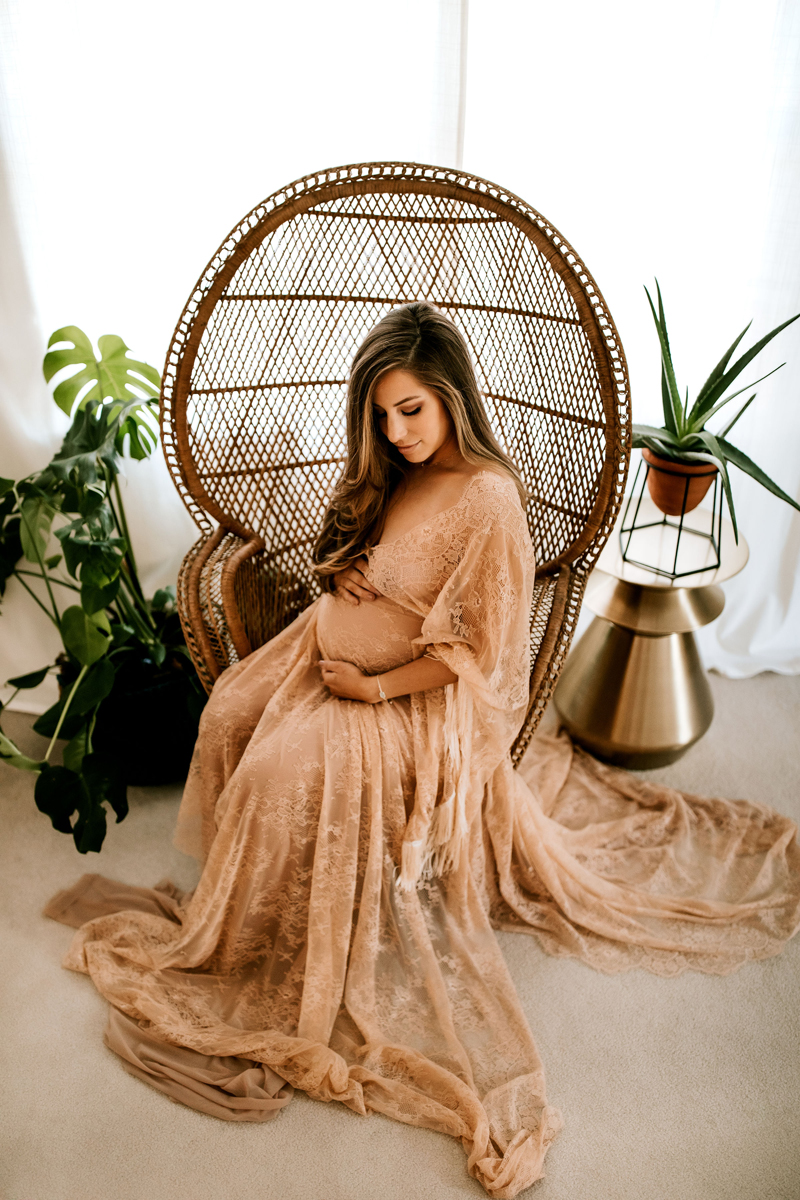 Atlanta Maternity Photographer, a woman sits looking at her pregnant belly in a large wicker chair