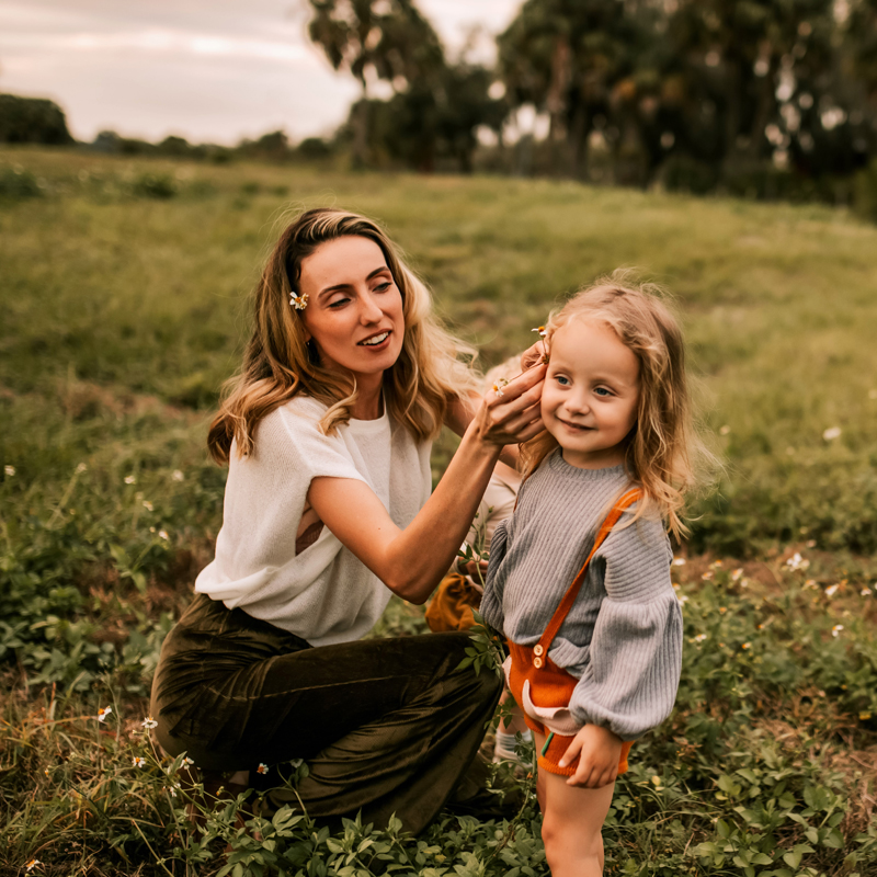 Atlanta Family Photographer, mother fixes flowers into daughters hair in a grassy field