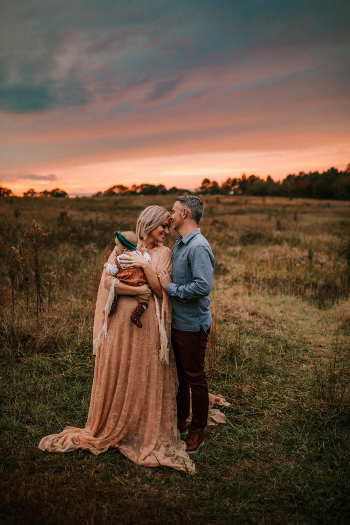 Photographer Mentorships, couple standing in a field together with their baby
